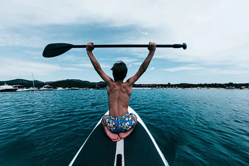 Homme pratiquant le stand-up paddle en mer, vue dorsale, ciel nuageux