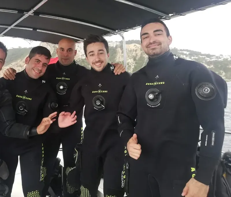 Quatre plongeurs souriants en combinaison complète sur un bateau
