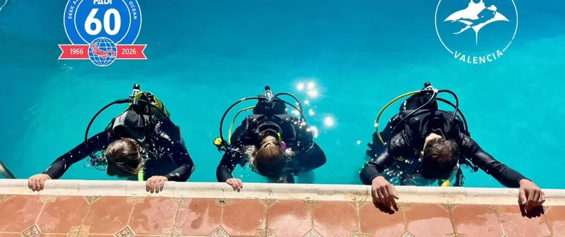 Trois plongeurs en équipement complet au bord d'une piscine bleue