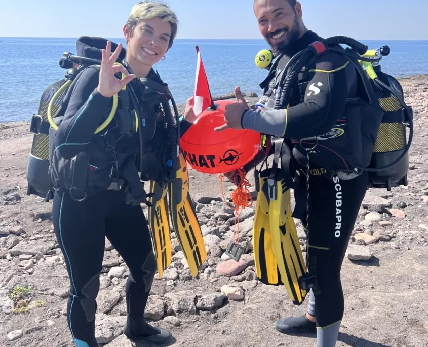 Deux plongeurs souriants avec leur équipement sur une plage rocheuse