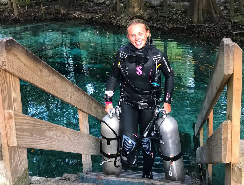 Plongeuse souriante avec deux bouteilles sur des marches en bois