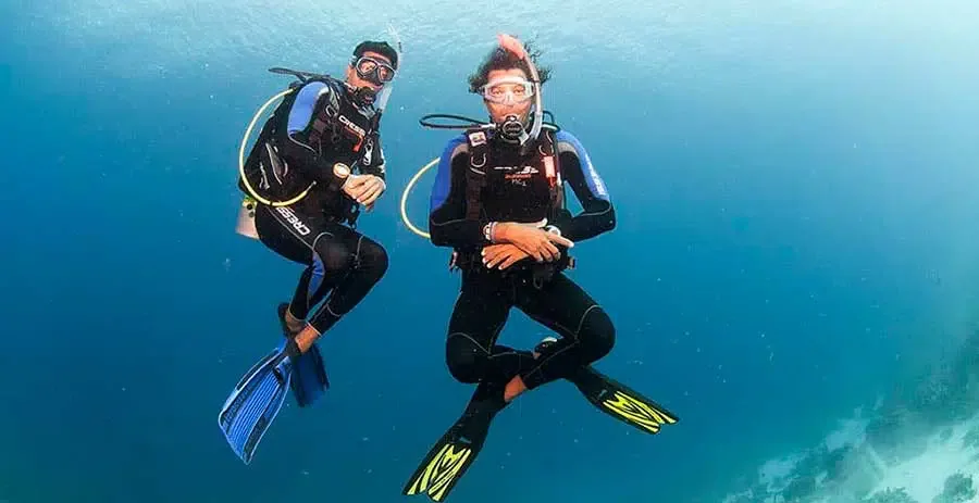 Deux plongeurs en combinaison flottent dans une eau bleue claire