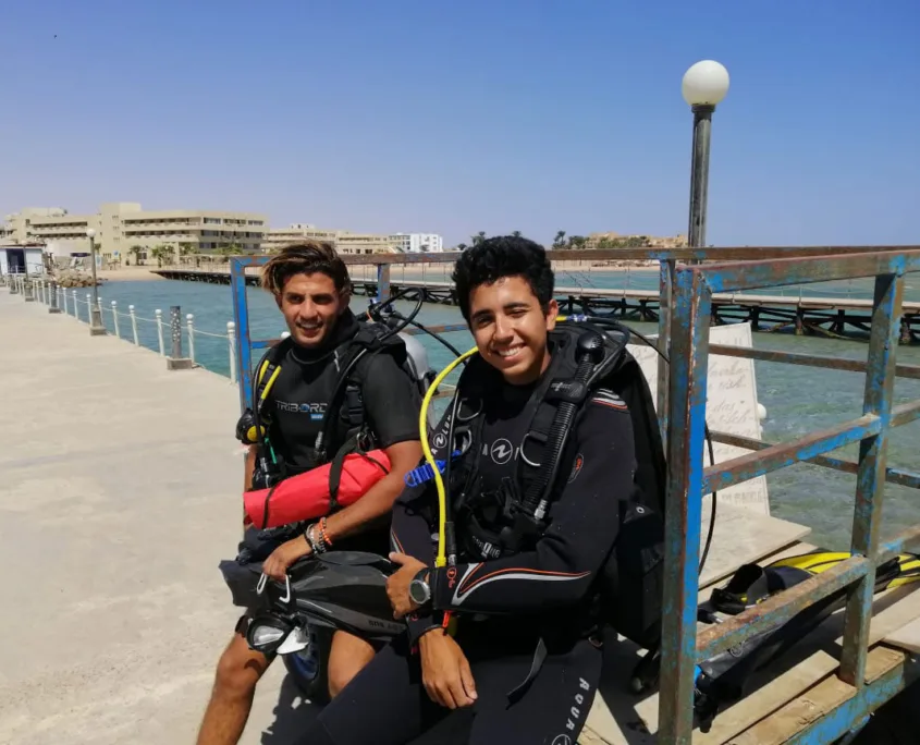 Deux plongeurs souriants assis sur un ponton avec leur équipement