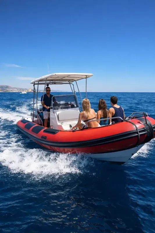 Bateau semi-rigide rouge en mer avec passagers, ciel bleu et côte