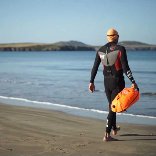 Une personne en combinaison de natation orange marche sur une plage