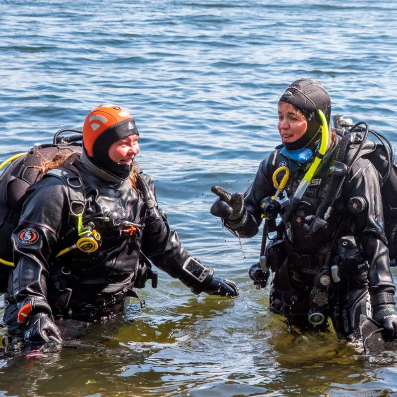 Deux plongeuses en combinaison discutent dans l'eau peu profonde