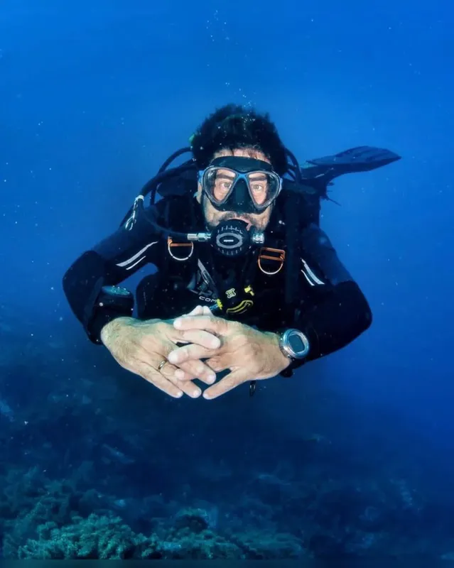 Plongeur en combinaison noire nageant sous l'eau, mains jointes, regardant la caméra