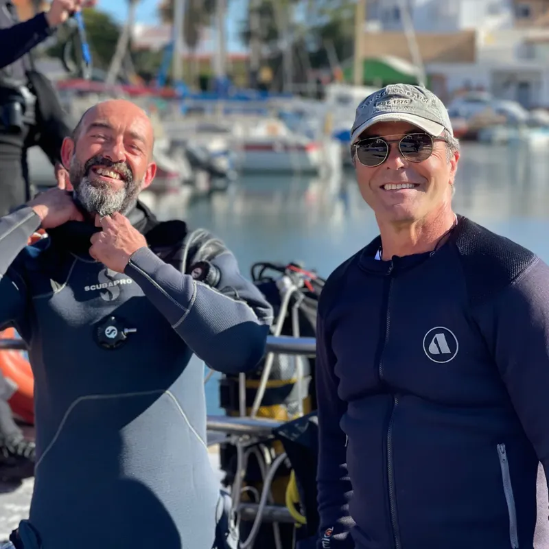 Deux hommes souriants, équipés pour la plongée, sur un bateau en mer