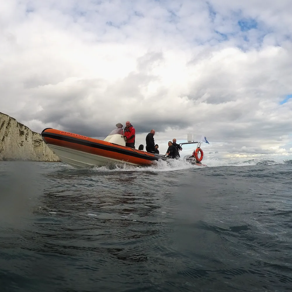 Bateau semi-rigide avec des plongeurs en mer, ciel nuageux et falaises