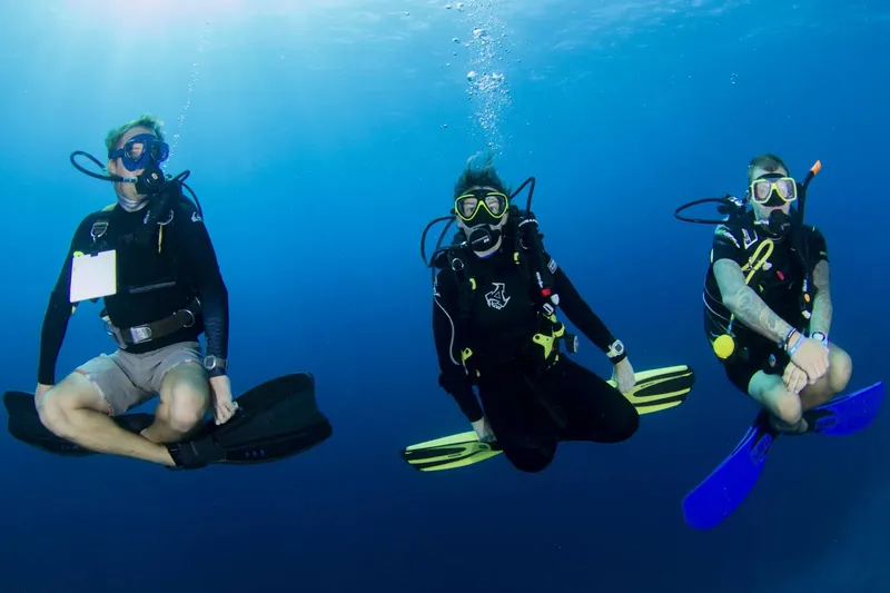 Trois plongeurs en combinaison flottent paisiblement dans l'eau bleue