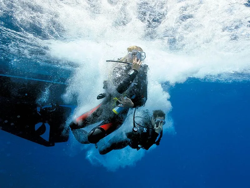 Deux plongeurs en combinaison s'immergent dans une eau bleue claire