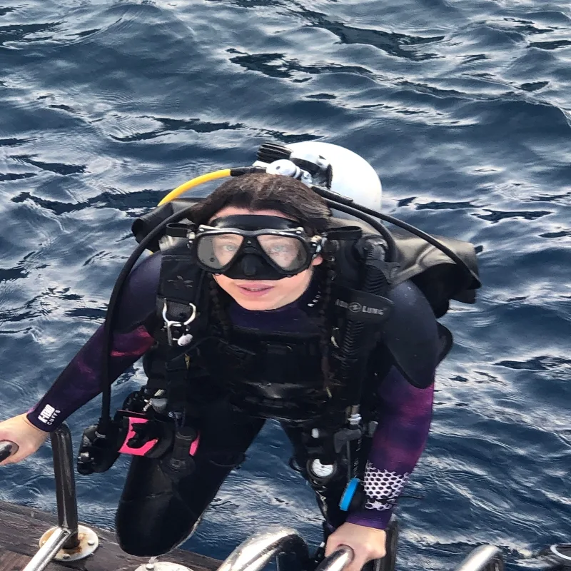 Plongeur équipé remonte sur un bateau, visage souriant et regard direct