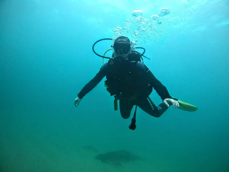 Plongeur en combinaison noire nageant dans une eau turquoise claire