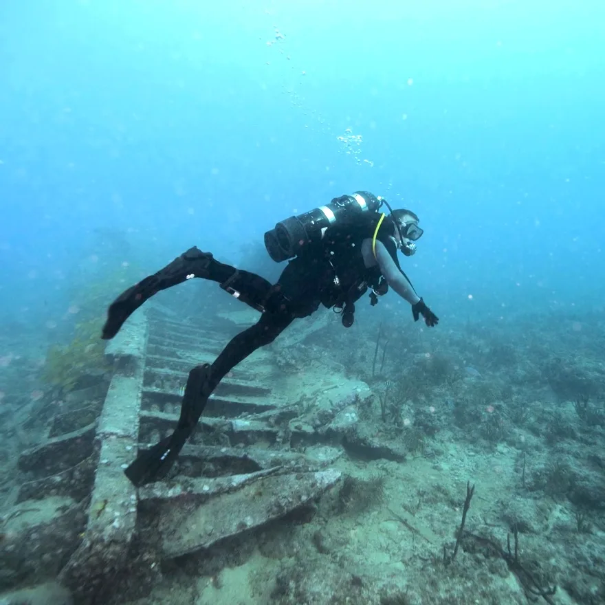 Plongeur en combinaison explore une épave sous-marine bleu clair