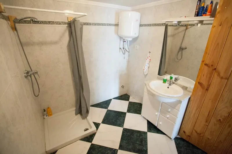Salle de douche avec carrelage, lavabo, douche et chauffe-eau blanc