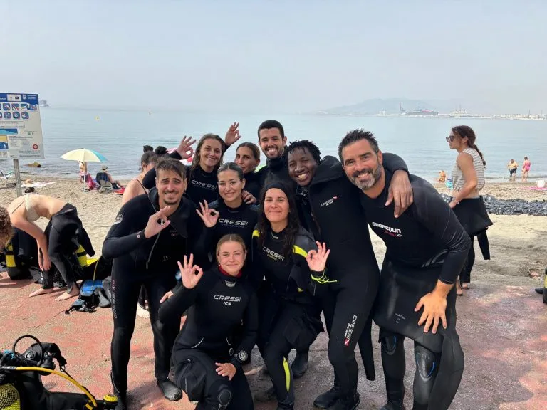 Groupe de plongeurs souriants en combinaison sur une plage ensoleillée