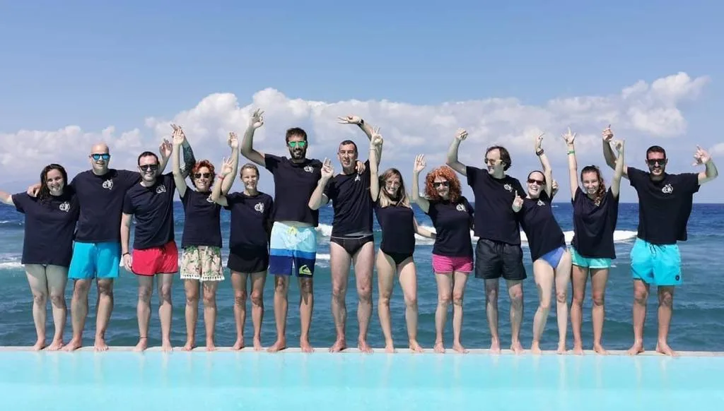 Groupe de personnes souriantes, bras levés, devant la mer bleue