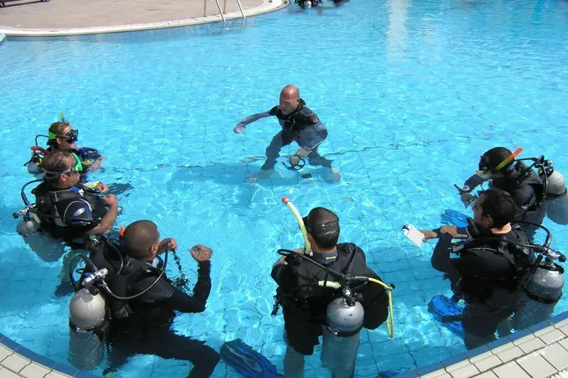 Groupe de plongeurs en formation dans une piscine, instructeur expliquant