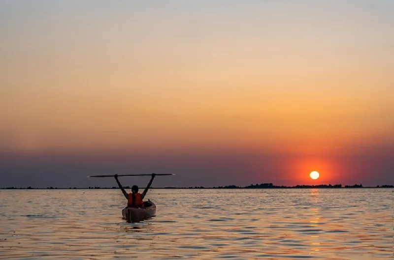 Kayak sur l'eau calme au coucher du soleil orangé et doré