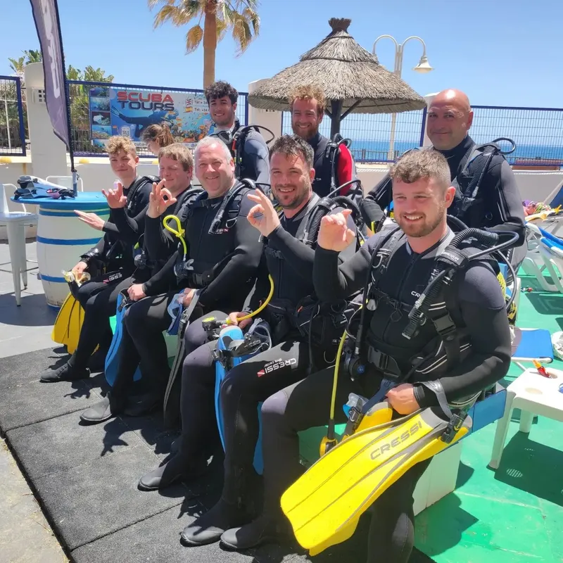 Groupe de plongeurs équipés souriant sur un ponton ensoleillé