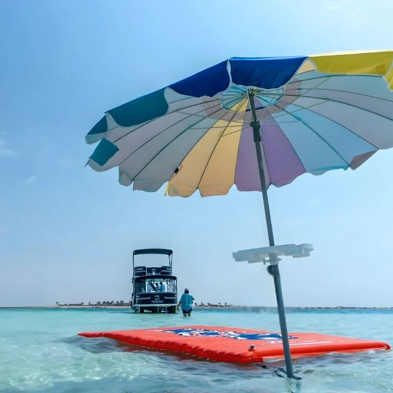 Plage turquoise, bateau de plongée au loin, parasol coloré et plateforme flottante