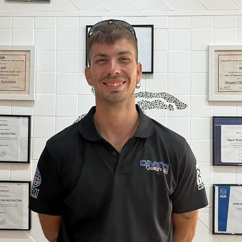 Un homme souriant porte un polo avec un logo de plongée