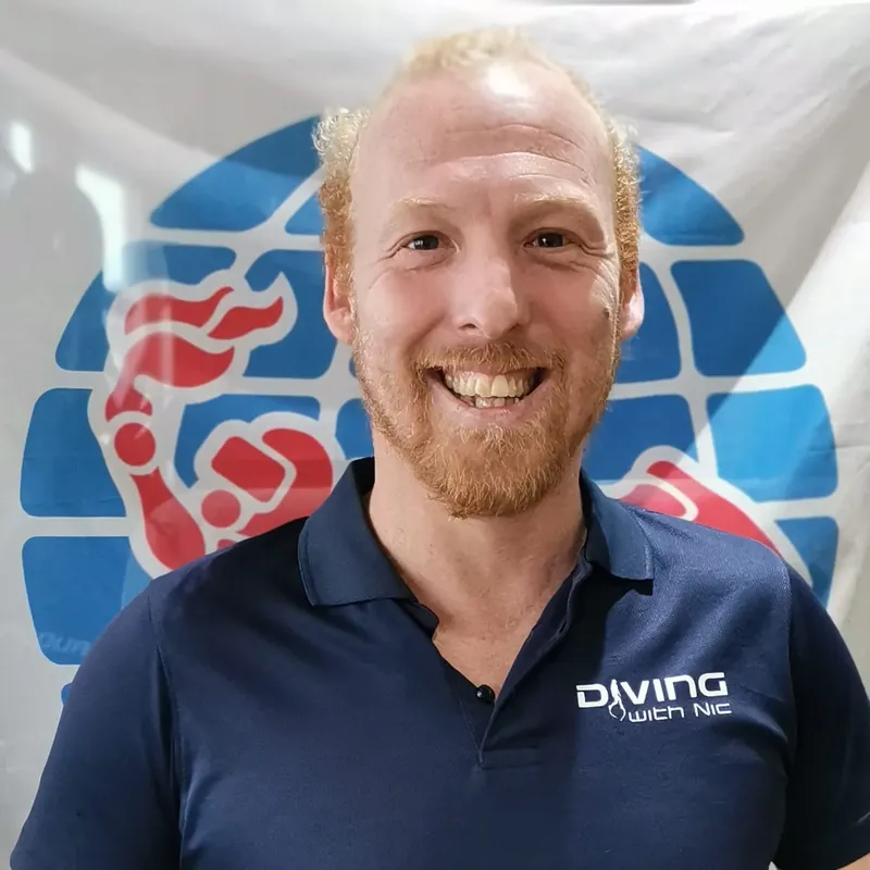 Homme souriant avec une barbe rousse portant un polo bleu