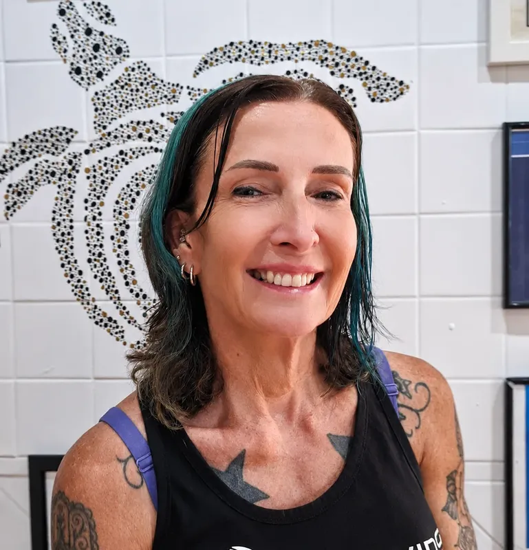 Femme souriante aux cheveux turquoise, tatouages visibles, fond carrelé