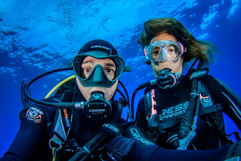 Deux plongeurs souriants avec leur équipement complet dans l'eau bleue