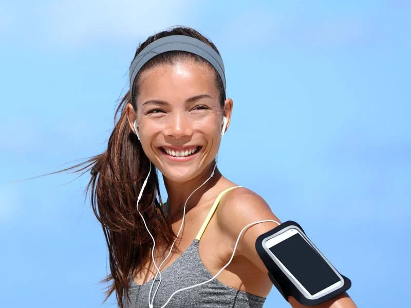 Jeune femme souriante avec des écouteurs et un brassard pour téléphone