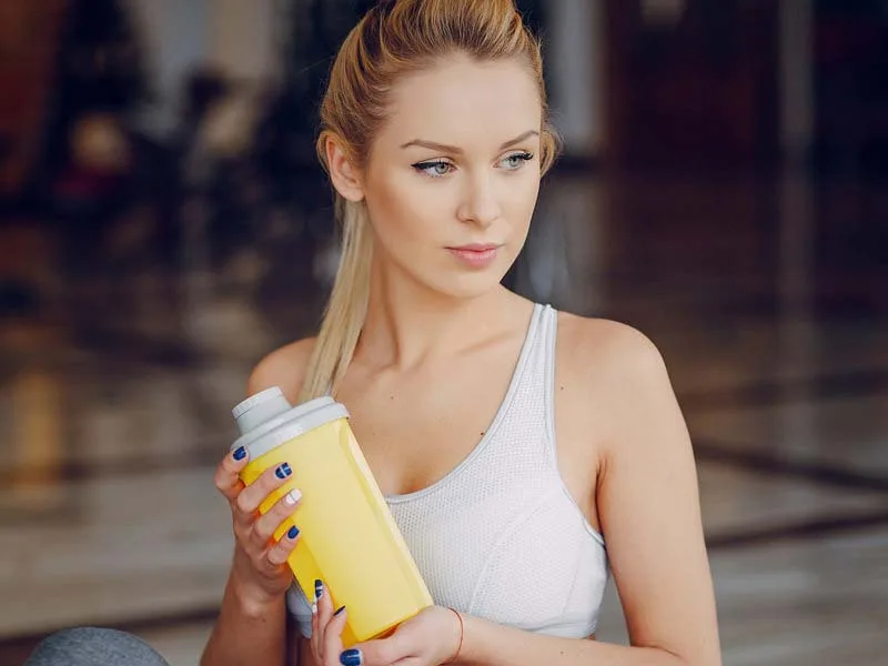 Jeune femme tenant une bouteille jaune, regard pensif, style de vie sain