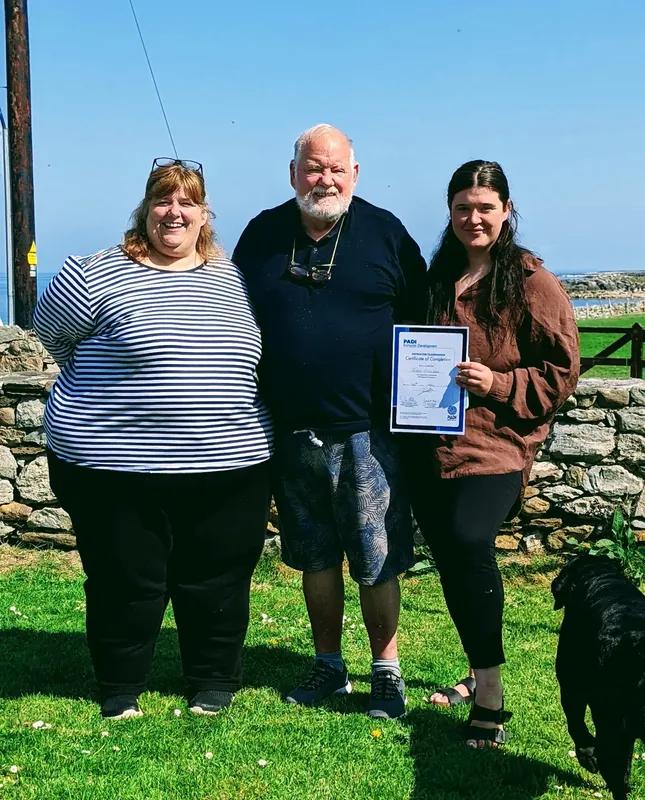 Trois personnes souriantes posent avec un certificat de plongée en extérieur