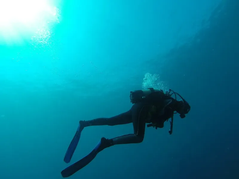 Plongeur en scaphandre nageant dans une eau bleue claire et ensoleillée
