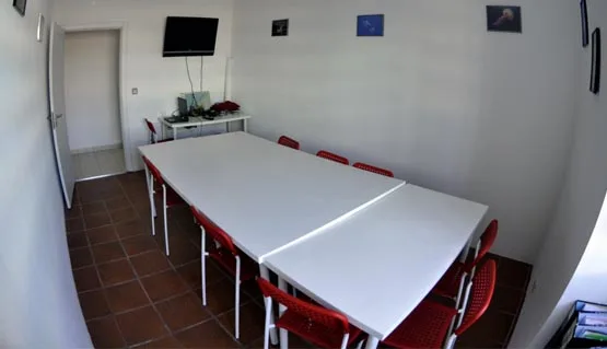 Salle de cours avec tables blanches et chaises rouges éclairée