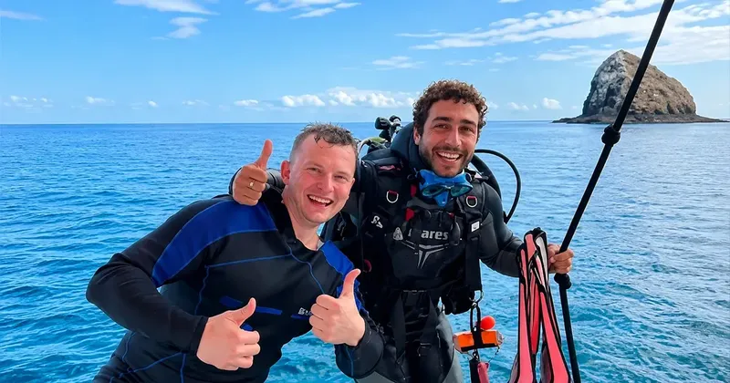 Deux plongeurs souriants font des pouces levés sur un bateau en mer