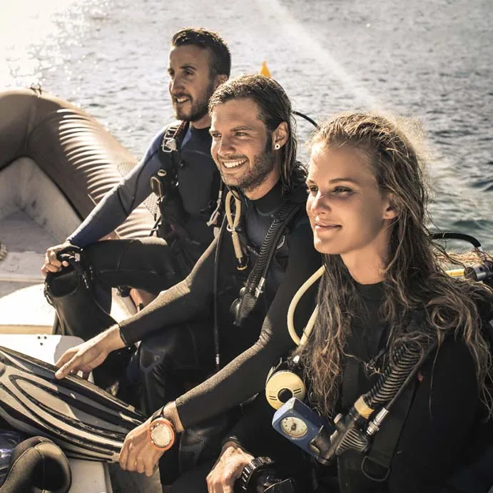 Trois plongeurs souriants équipés sur un bateau en mer