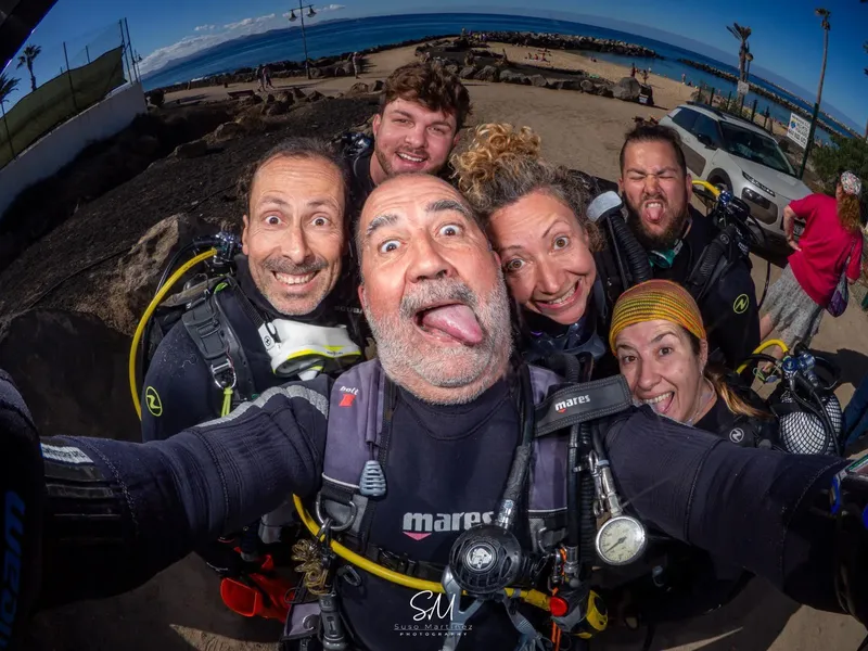 Groupe de plongeurs souriants et équipés sur un fond marin rocheux