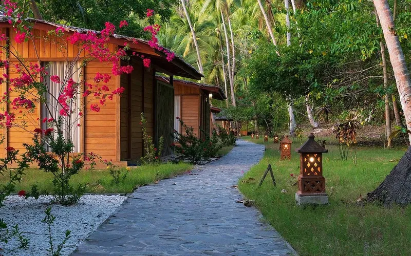 Allée pavée bordée de bungalows en bois et de végétation tropicale