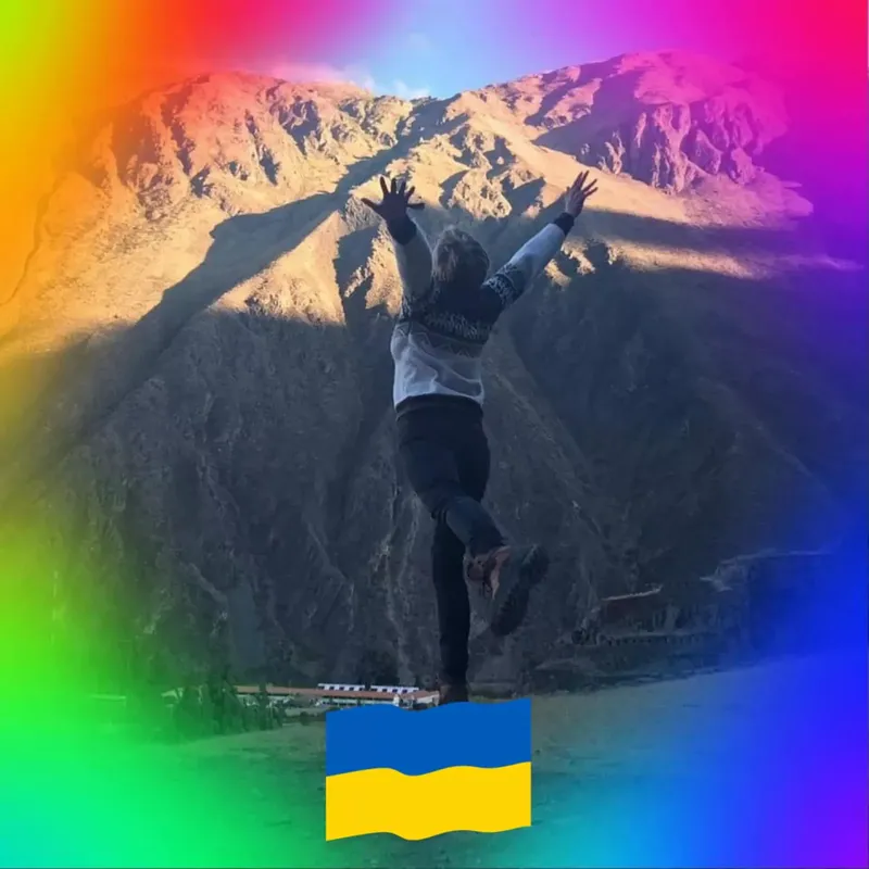 Personne sautant avec les bras levés devant un paysage montagneux et un drapeau