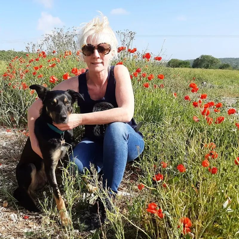 Femme souriante accroupie avec un chien dans un champ de coquelicots