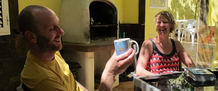 Deux personnes souriantes trinquent avec des tasses dans un espace extérieur