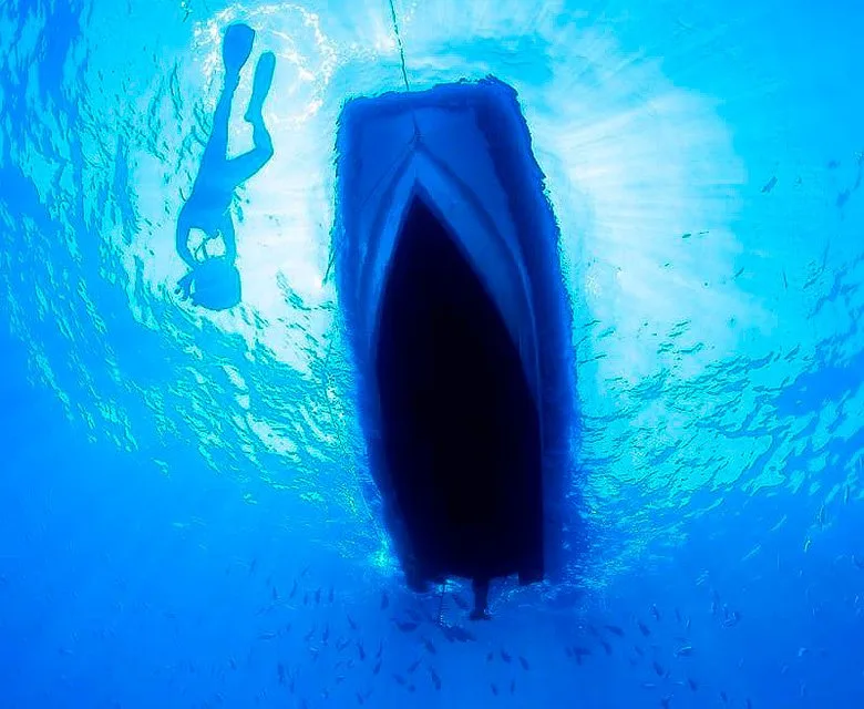 Plongeur observant la coque d'un bateau vu d'en bas dans l'eau