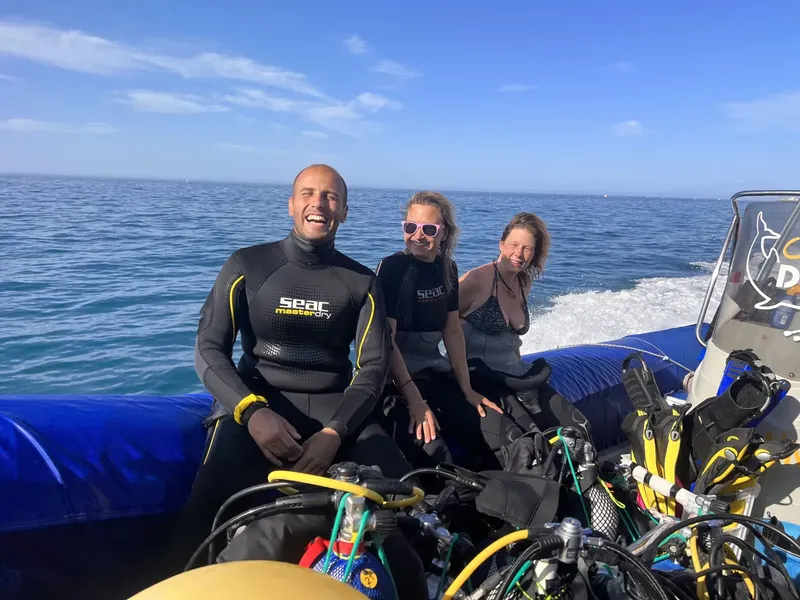 Trois plongeurs souriants assis dans un bateau semi-rigide bleu
