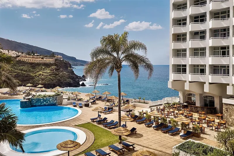 Vue d'un hôtel avec piscine, transats et la mer en arrière-plan