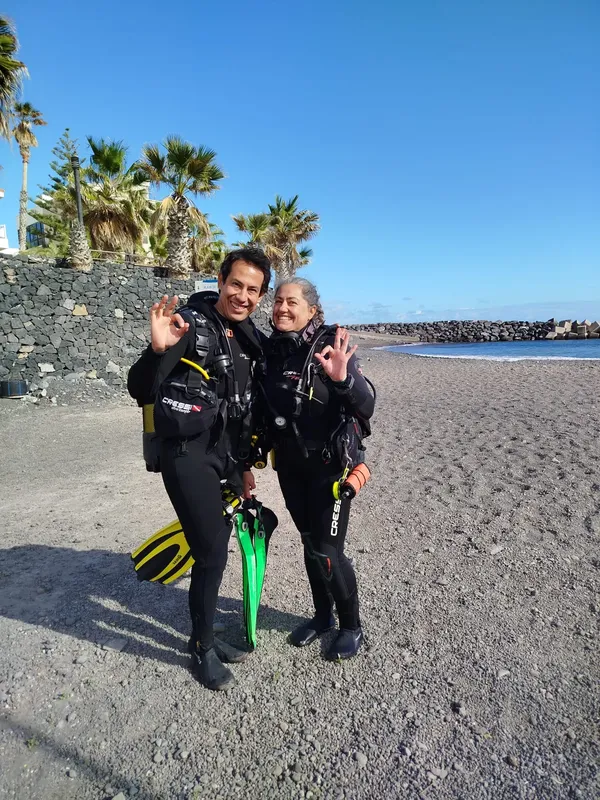 Deux plongeurs souriants en combinaison sur une plage de sable noir