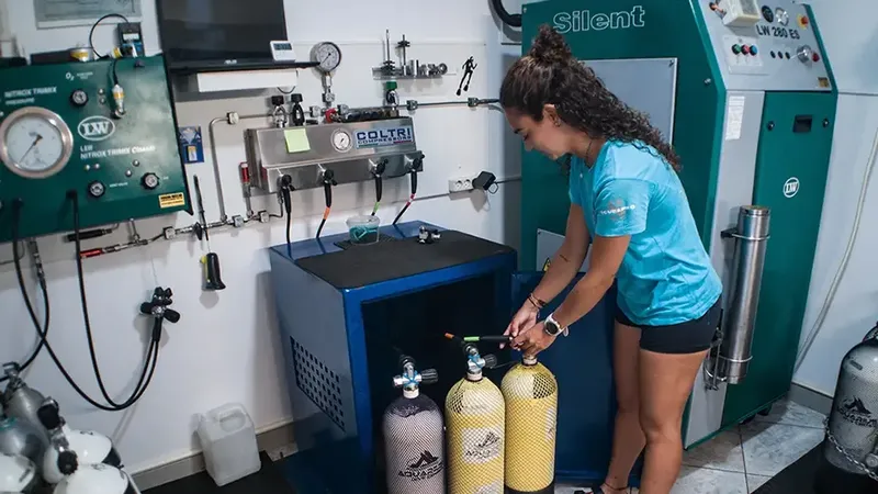 Une femme manipule des bouteilles de plongée dans un atelier de compression