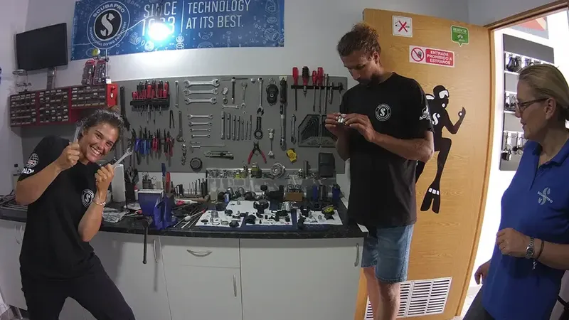 Trois personnes travaillent sur du matériel de plongée dans un atelier