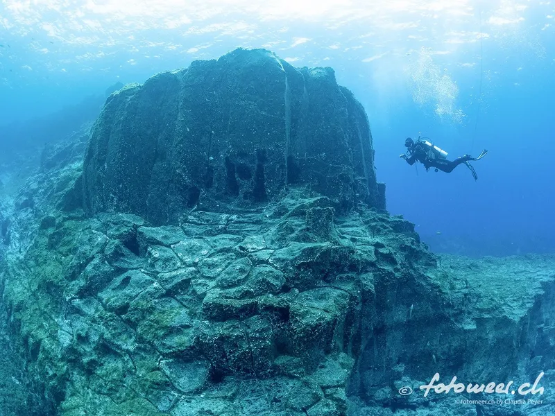 Plongeur explorant une formation rocheuse sous-marine dans une eau claire
