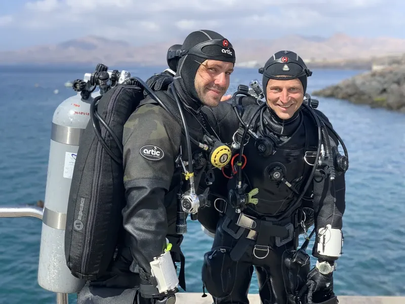 Deux plongeurs souriants équipés sur un ponton ensoleillé