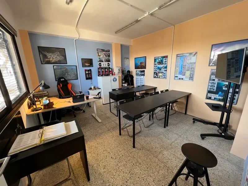Salle de cours avec bureaux, chaises, posters et un instructeur assis